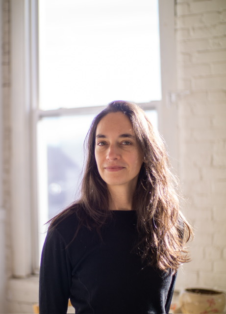 Julia's long hair flows over her shoulder as she stands, backlit, in front of a bright window.