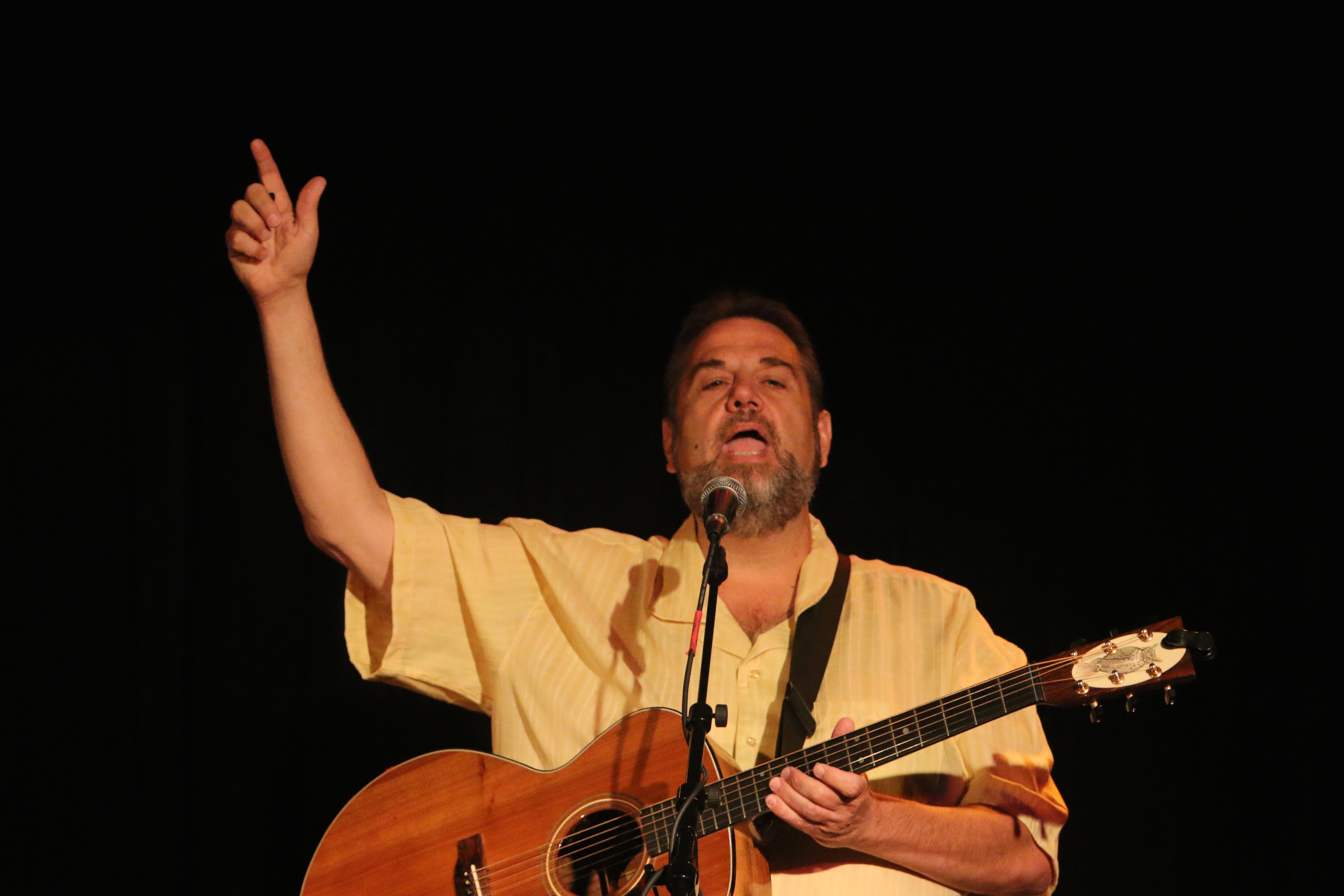 Matt points to the sky with one hand while full-throated singing and playing his guitar.